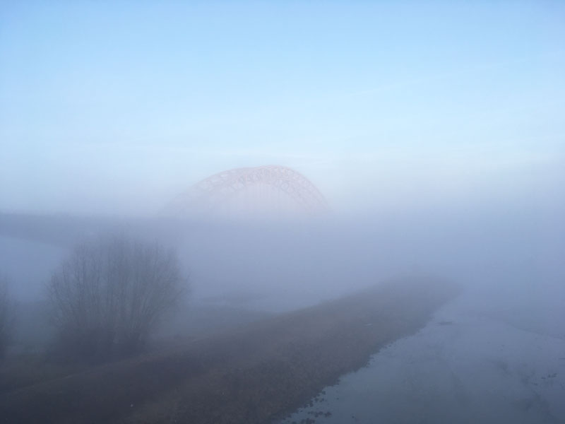Die Brücke über die Waal schimmert in der Morgensonne über den Nebelbänken