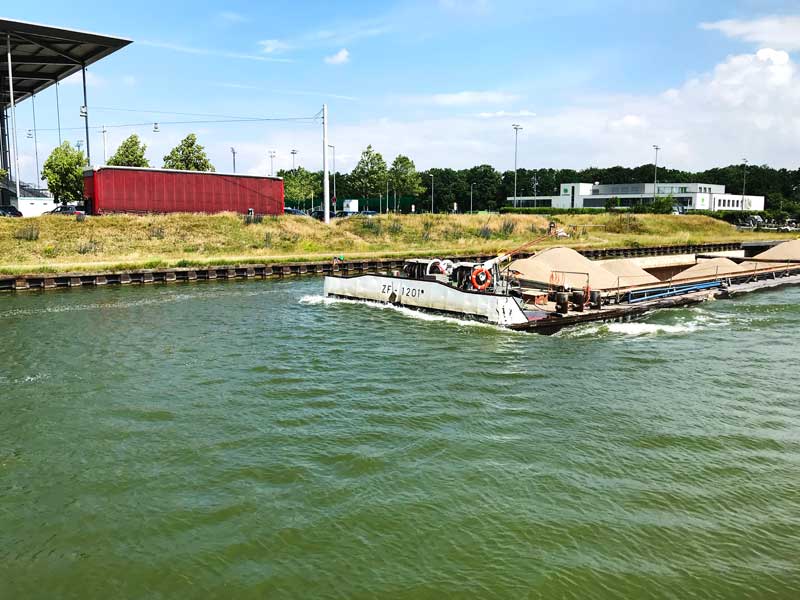 Direkt vor uns passiert ein Frachtschiff die schmale Hafeneinfahrt. Links ist noch das Dach der Volkswagenarena zu sehen, rechts hinten die Geschäftsstelle des VfL Wolfsburg