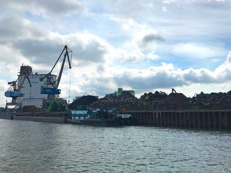 Ein Frachtschiff liegt im Hafen Braunschweig am Quai und wird mit großen Kränen mit Metallschrott beladen