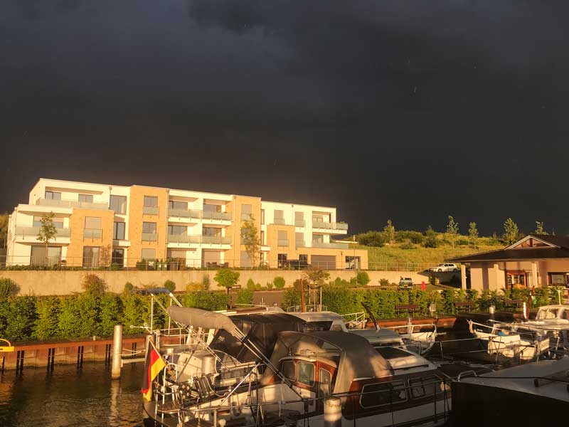 Vor tiefschwarzem Himmel sind die Gebäude hinter der Marina Bortfeld und die Boote in helles, goldenes Sonnenlicht getaucht