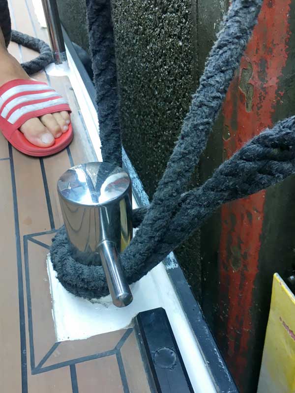 An der Klampe in der Mitte des Boots ist die Leine mit einem Auge befestigt. Die Leine wird um den Poller der Schleuse herumgeführt und dann noch einmal mit einer Schlaufe über den Poller gelegt.