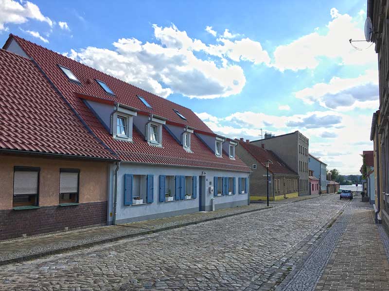 Straße in Ketzin Havel, die mit altem, holprigem Kopfsteinpflaster belegt ist. Zu beiden Seiten stehen niedrige alte, schön renovierte Wohngebäude