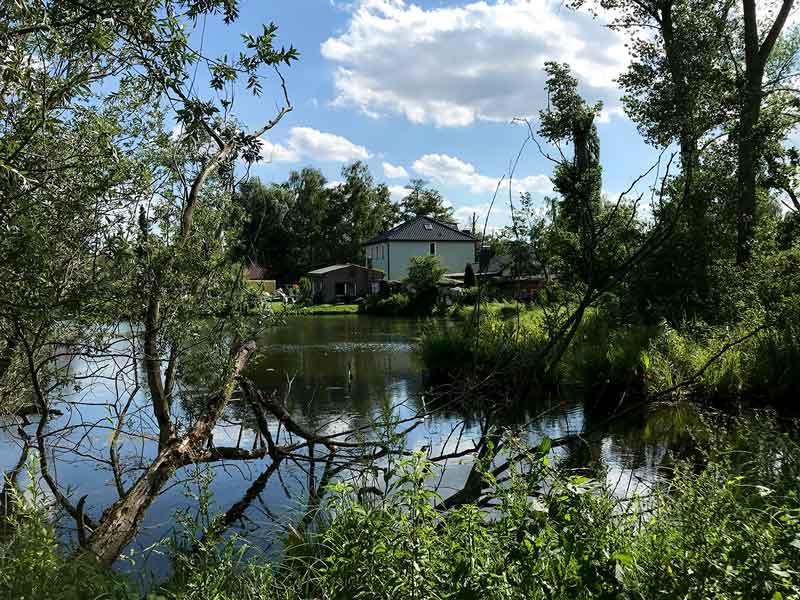 Blick übers Wasser auf ein Haus der Kliemsiedlung in Ketzin Havel, wild und verwunschen