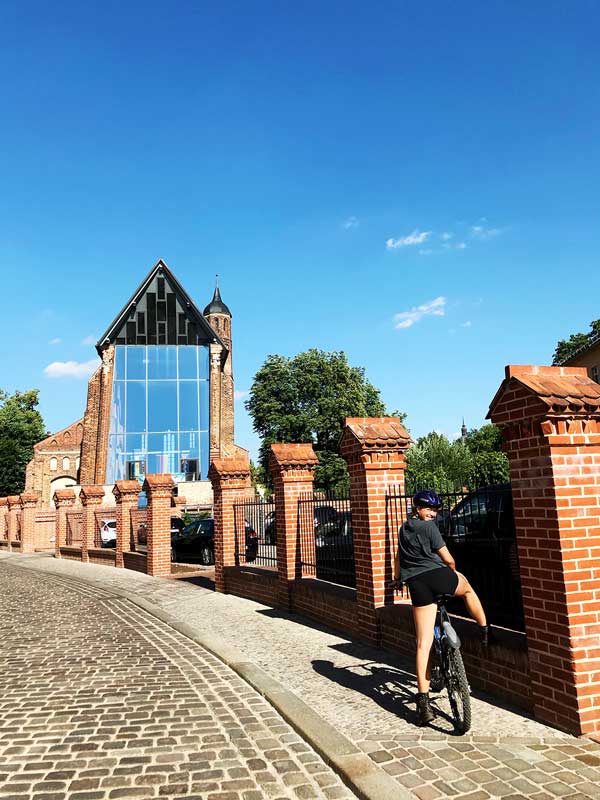 Das Mädchen sitzt auf dem Rad und dreht sich zu mir um. Im Hintergrund die Johanniskirche in Brandenburg an der Havel.