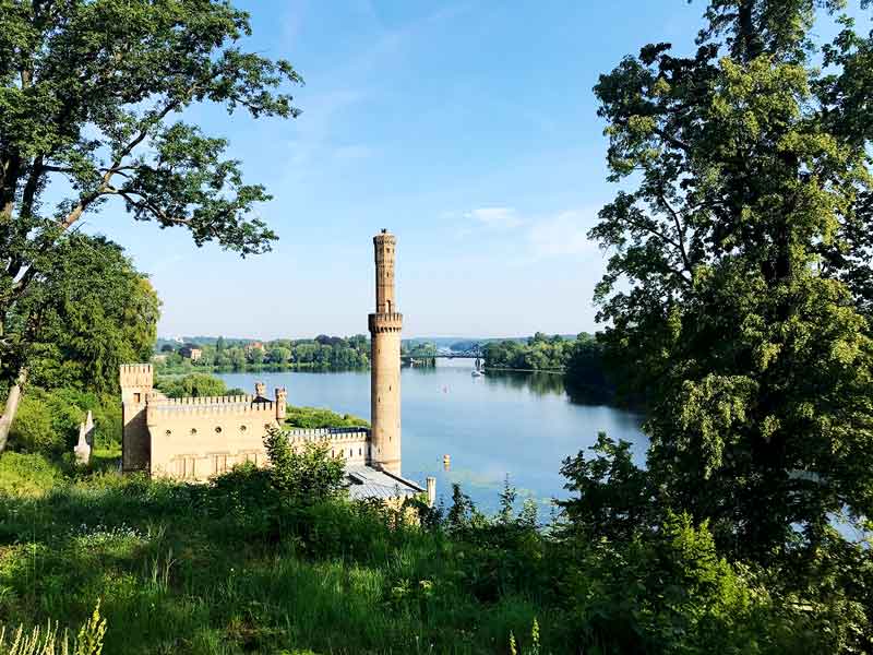 Blick von einer Anhöhe auf das alte Dampfmaschinenhaus im Park Babelsberg in Potsdam mit Glienicker Brücke im Hintergrund
