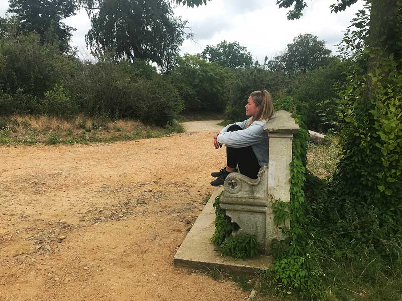 Die junge Frau sitzt auf einer alten Steinbank am Flatowturm und blickt über den Park Babelsberg in Potsdam an der Havel