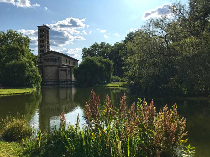 Die Friedenskirche im italienischen Stil mit Campanile an einem See mit Schilf und Bäumen im Park Sanssouci in Potsdam