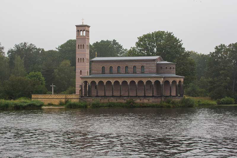 Am Ufer des Jungfernsee bei Sacrow in der Nähe von Potsdam liegt die italienisch anmutende Heilandskirche mit der gestreiften Fassade und den Bögen des Laubengangs direkt am Wasser