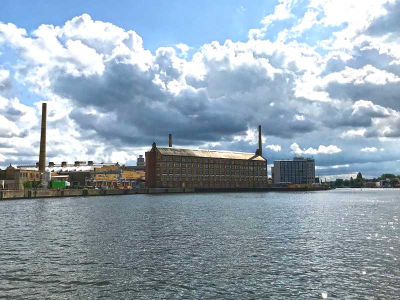 Gut erhaltenes altes Industriegebäude mit Schloten an der Spree in Oberschöneweide in Berlin, dahinter dramatische Wolken