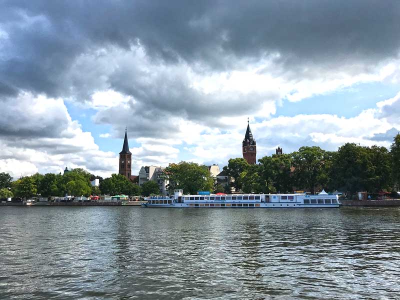Stadtansicht von Köpenick bei Berlin vom Wasser aus mit Stadthafen und prägnanten Gebäuden Rathaus und Sankt Laurentiuskirche, im Vordergrund ein langes, niedriges Passagierschiff