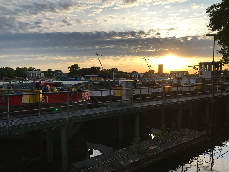 Die Sonne geht hinter alten Lastkähnen am Ufer der Rummelburger Bucht an der Spree in Berlin unter