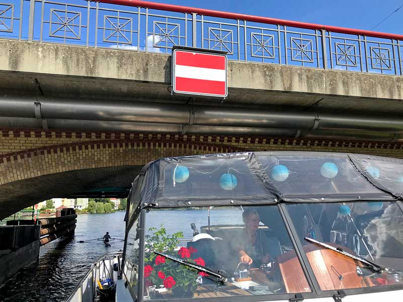 Blick vom Bug aus auf den Steuerstand und die Brücke: Barbara steuert das Boot unter einer niedrigen Brücke hindurch - Lange Brücke auf der Spree in Köpenick bei Berlin