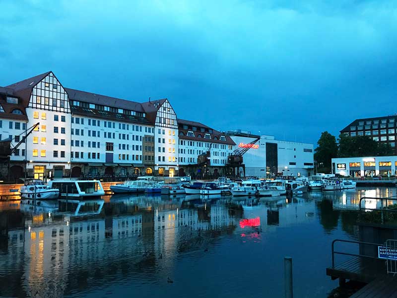 Blick auf das ehemalige Lagerhaus des Tempelhofer Hafens in Berlin in der Abenddämmerung. Die Lichter der Geschäfte und Restaurants spiegeln sich im Wasser des Hafenbeckens