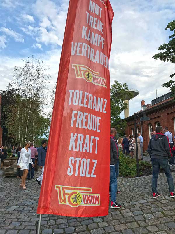 Fahne von Union Berlin vor einem Veranstaltungsgebäude im Marienpark in Berlin Mariendorf, die auf eine Veranstaltung des Fußballclubs hinweist. Die Gäste sind teilweise schick gekleidet
