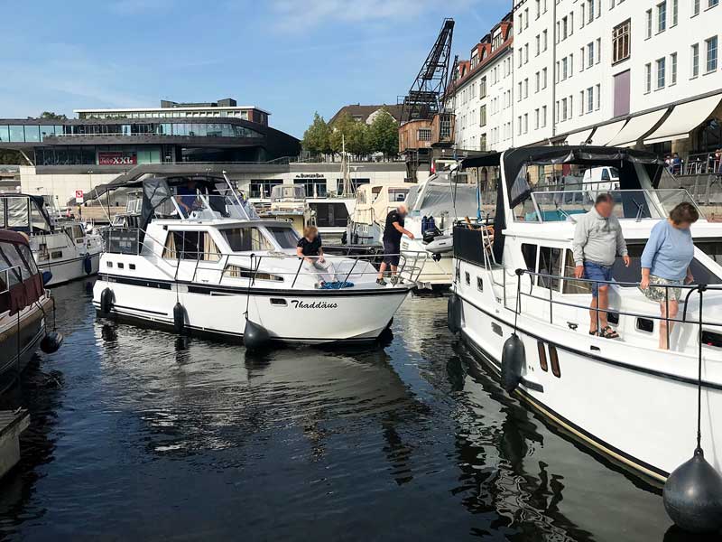 Mann auf Charteryacht hält mittels eines Bootshakens Abstand von einem anderen Boot im Tempelhofer Hafen Berlin