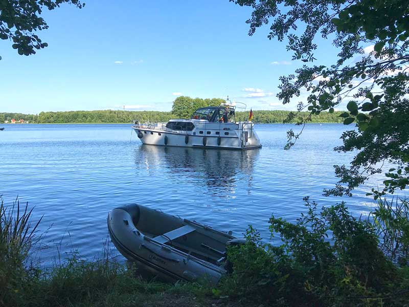 Die Motoryacht liegt unweit des Ufers vor Anker, im Vordergrund das Beiboot, im Klein Köriser See, Teil der Dahme-Wasserstraße und der Teupitzer Gewässer in Brandenburg, südlich von Berlin