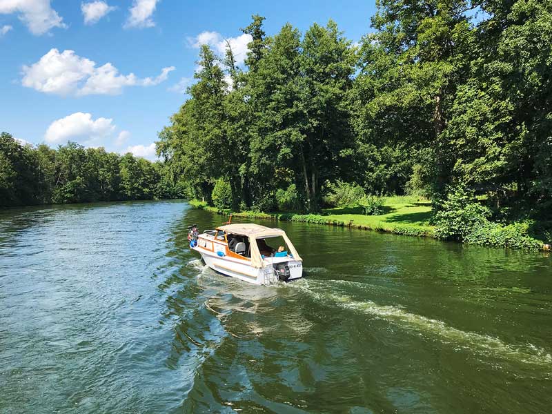 Vor uns fährt ein kleines Sportboot auf der Dahme, die die Seen der Seenkette verbindet. Dahme-Wasserstraße, Brandenburg, südlich von Berlin