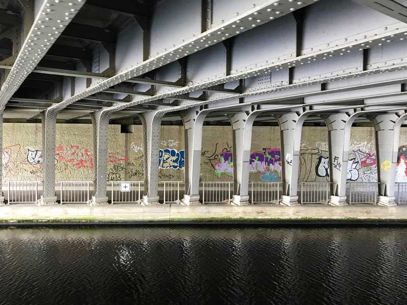 Unter einer Stahlbrücke über den Teltowkanal in Berlin mit Stahlträgern und Grafitti