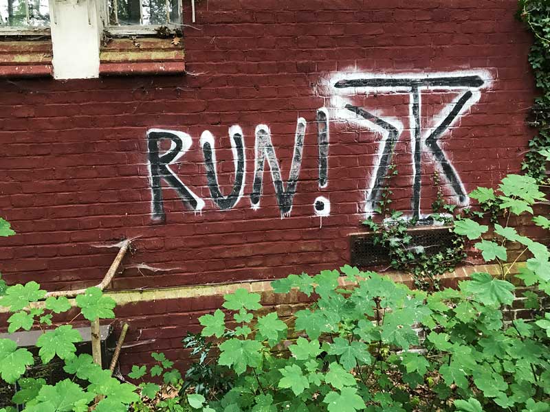 Ein Grafitto RUN! auf dunkelrotem Mauerwerk in der Landesirrenanstalt Teupitz, Brandenburg, südlich von Berlin - Lost Places
