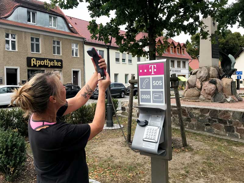 Frau hält den Hörer eines öffentlichen Münzfernsprechers, als wollte sie ein Selfie machen - Teupitz, Brandenburg