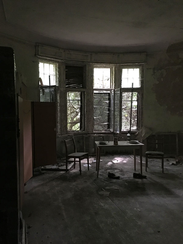 Ehemaliges Verwaltungsgebäude der Landesirrenanstalt Teupitz, Brandenburg, südlich von Berlin. Auf einem Tisch stehen zwei Teller und eine Flasche, davor auf dem Boden Schuhe. Lost Places