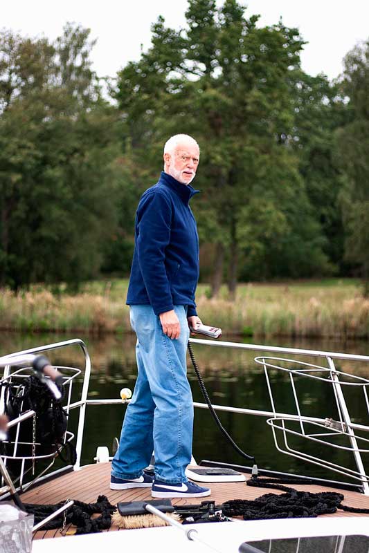 Mein Vater steht am Bug des Boots und holt mit der elektrisch bedienten Ankerwinde den Anker ein