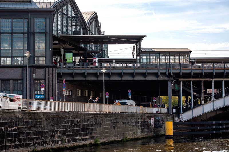Am Ufer der Spree in Berlin erhebt sich linkerhand der Bahnhof Friedrichstraße mit seiner schönen Stahl-Glas-Konstruktion