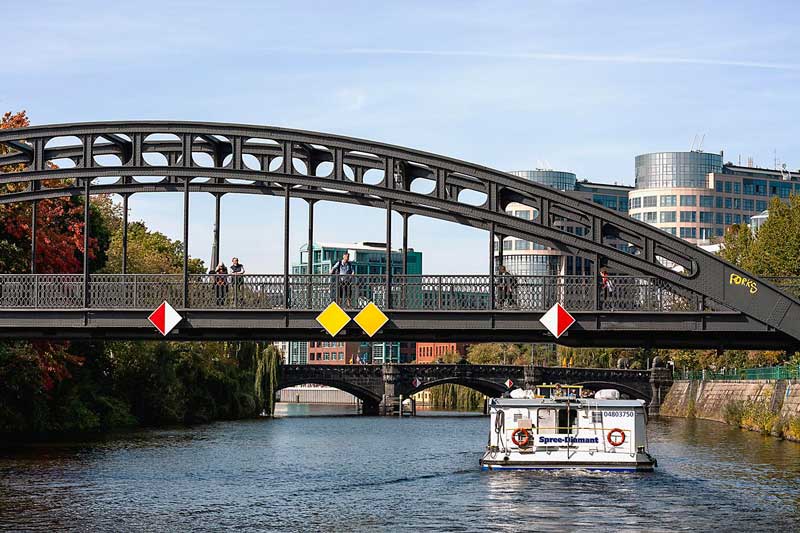 Über die Spree in Berlin erstrecken sich zwei Brücken, der Gerickesteg im Vorder- und die Moabiter Brücke in Hintergrund, vor uns ein Ausflugsschiff