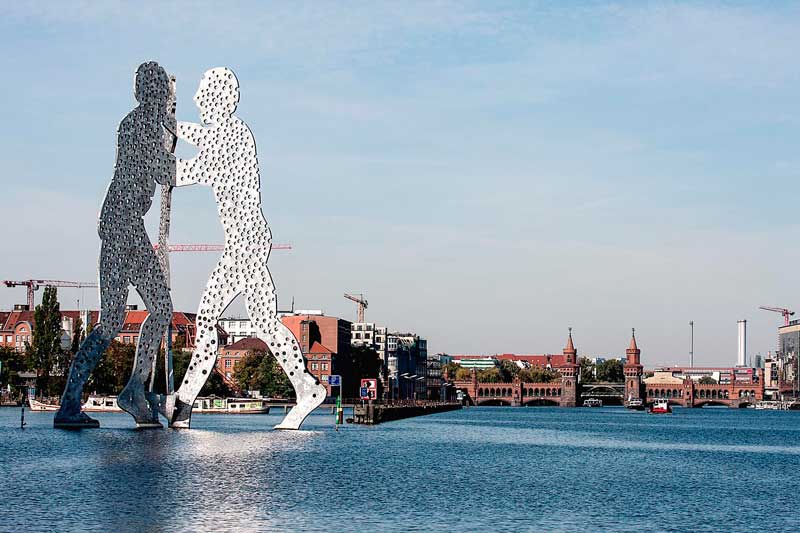 Die riesige silberne Skulptur, die am zwei Männer zeigt, steht am Osthafen Berlin in der Spree