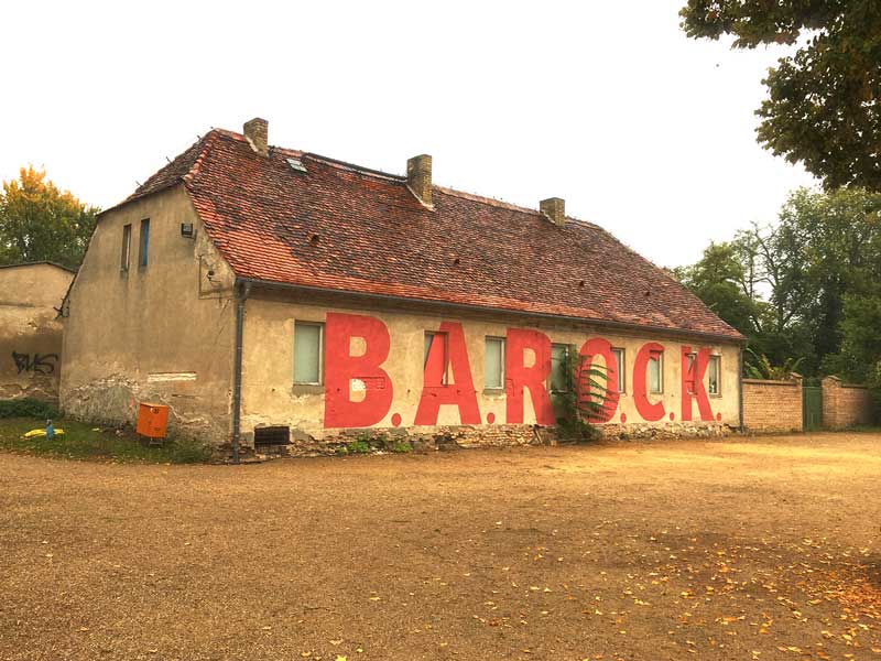 Der Titel der Ausstellung B.A.R.O.C.K. im Schloss Caputh, Brandenburg, ist mit riesigen roten Buchstaben auf eine alte Remise im Eingangsbereich gestrichen